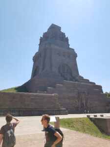 Außenaufnahme seitlich vom Völkerschlachtdenkmal. Riesiges monumentales, steinernes Gebäude, das sich verjüngend von einem breiten Sockel aufragt.