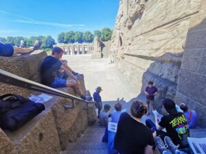 Die Gruppe der Exkursionsteilnehmenden vor dem Völkerschlachtdenkmal auf einer Treppe. Herr Dietrich im Vortrag begriffen.