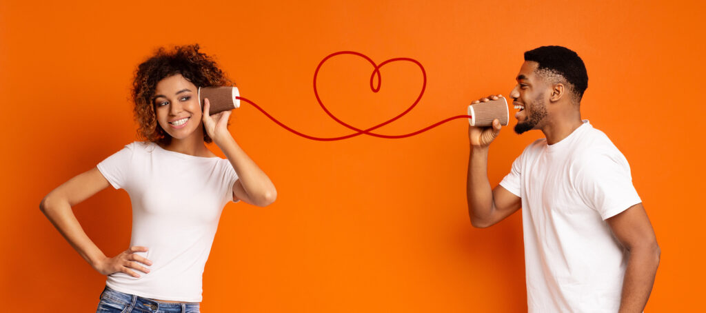 Communication and fun. Young black couple talking through tin can phone, orange background, panorama